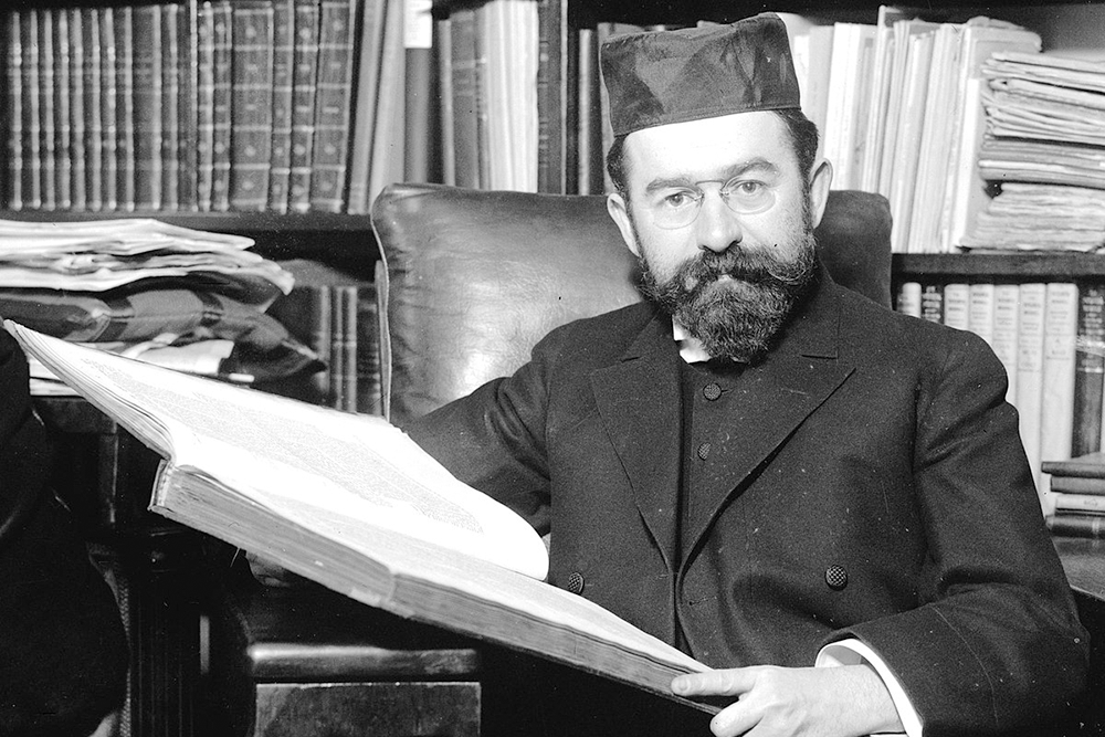 Historic photograph of a Chief Rabbi seated at his desk with an open book
